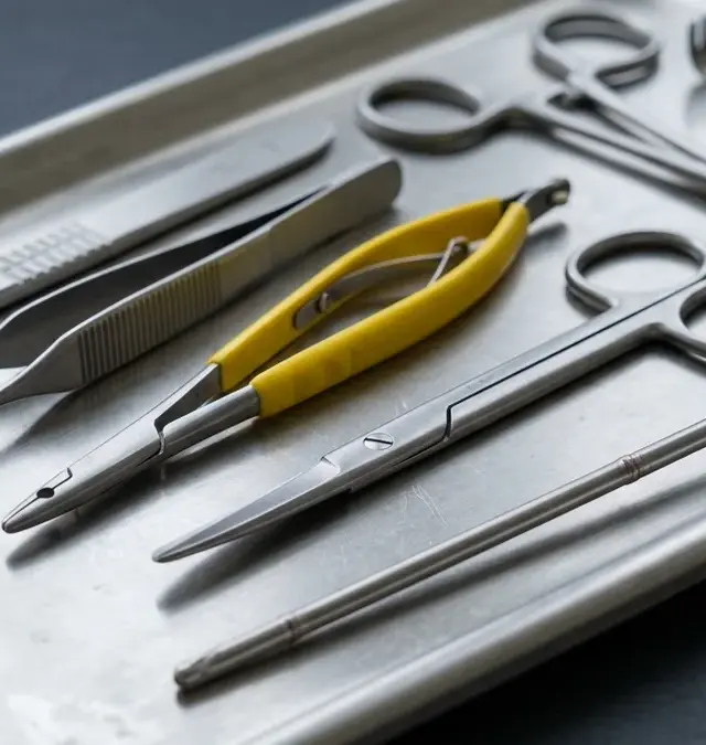 Nahaufnahme eines sterilen Instrumententabletts mit chirurgischen Instrumenten aus Edelstahl: Skalpell, Pinzette, Nadelhalter, Schere und Schaftinstrument
