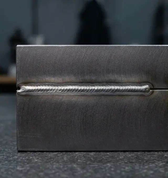 Macro image of a precise laser weld seam on mold steel with a yellow fixture handle in an inspection room Macro image of a precise laser weld seam on mold steel with a yellow fixture handle in an inspection room